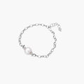 Rhodium-plated silver chain bracelet with single white freshwater pearl and heart charm clasp on cream background