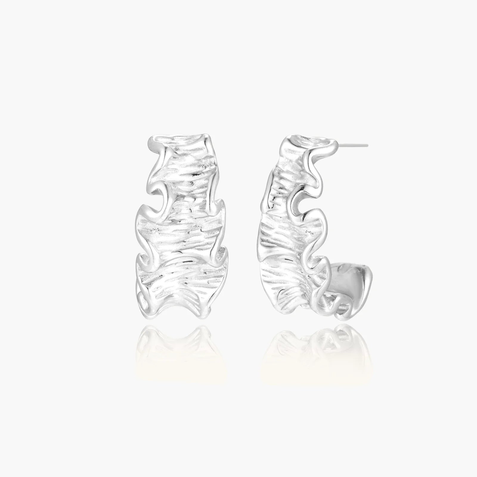 White gold plated sculptural hoop earrings with organic wavy edges and reflective metallic finish on cream background