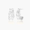 White gold plated sculptural hoop earrings with organic wavy edges and reflective metallic finish on cream background