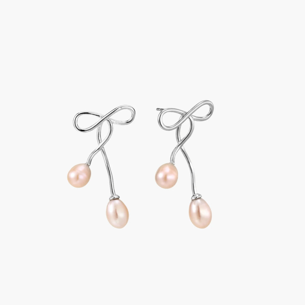 Rhodium-plated silver earrings with organic vine curves and two peachy freshwater pearls on cream background