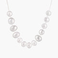 Graduated pearl-finish silver discs forming an organic bubble bib necklace on delicate chain against cream background.