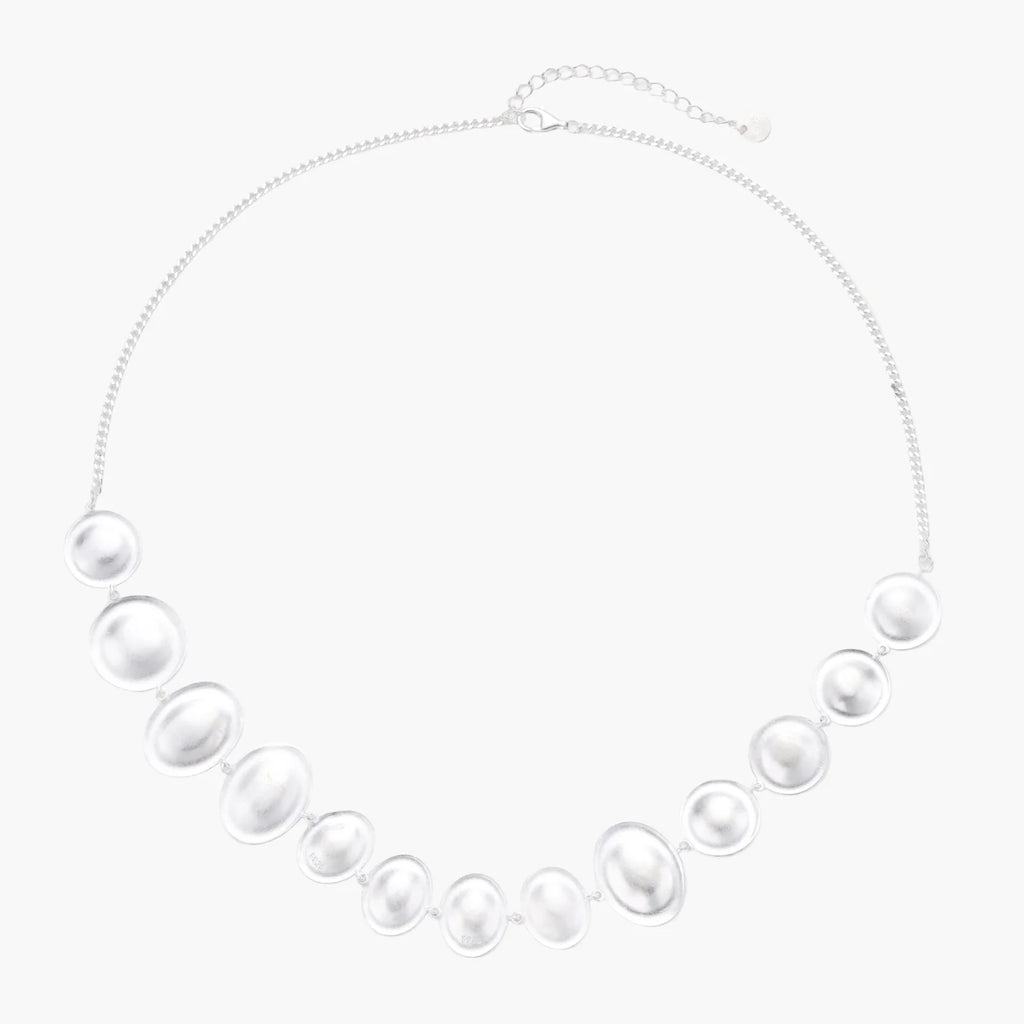 Graduated pearl-finish silver discs forming an organic bubble bib necklace on delicate chain against cream background.