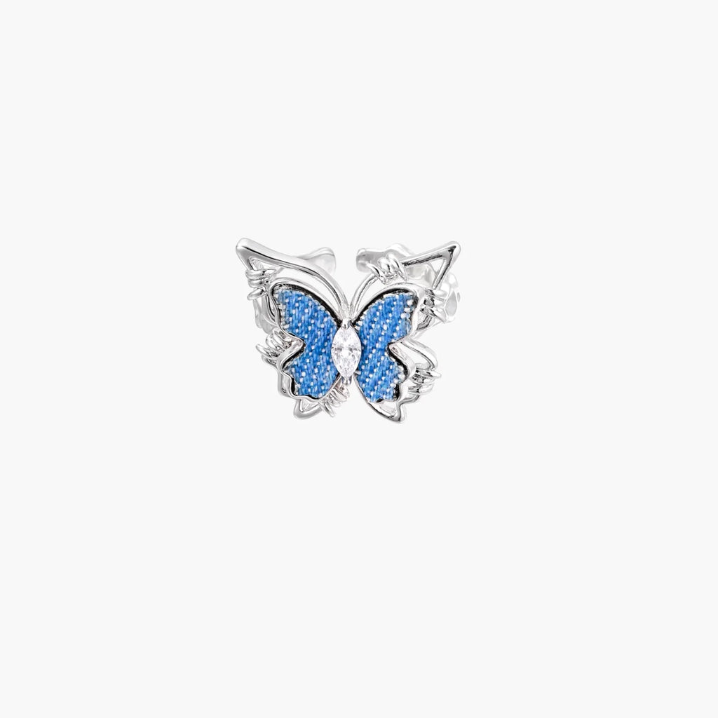 Silver-toned ring with blue denim butterfly wings, marquise zirconia center, and ornate scrollwork band on white background