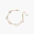 Double-strand gold bracelet with irregular baroque pearls and smooth freshwater pearls on cream background.