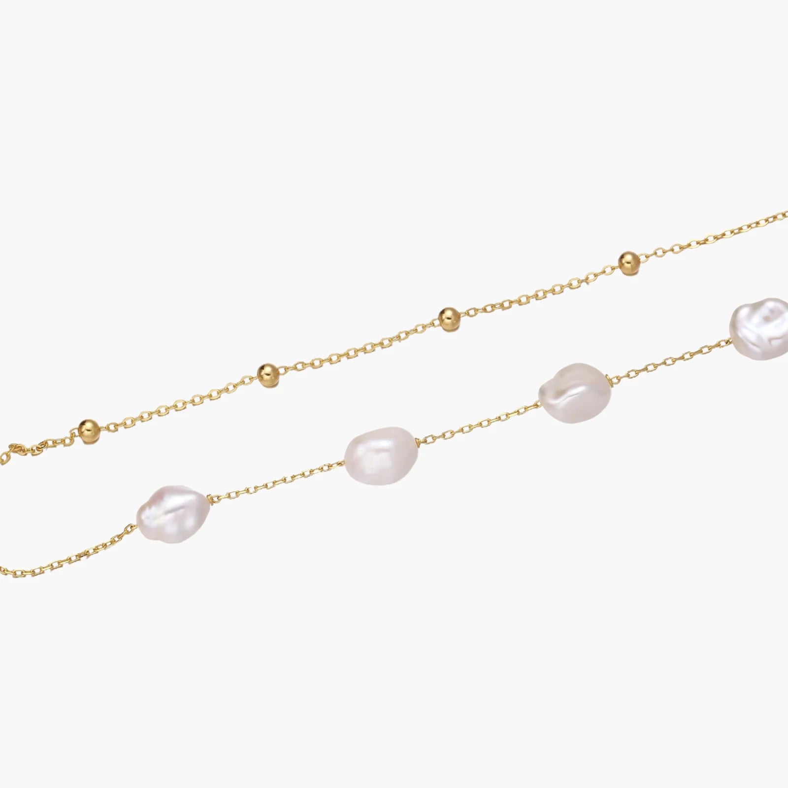 Double-strand gold bracelet with irregular baroque pearls and smooth freshwater pearls on cream background.