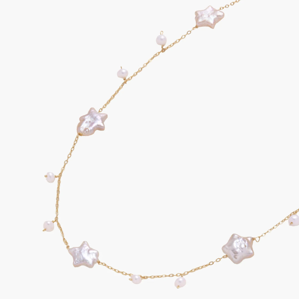 Gold vermeil chain with iridescent star-shaped baroque pearls and small round freshwater pearl drops on cream background.