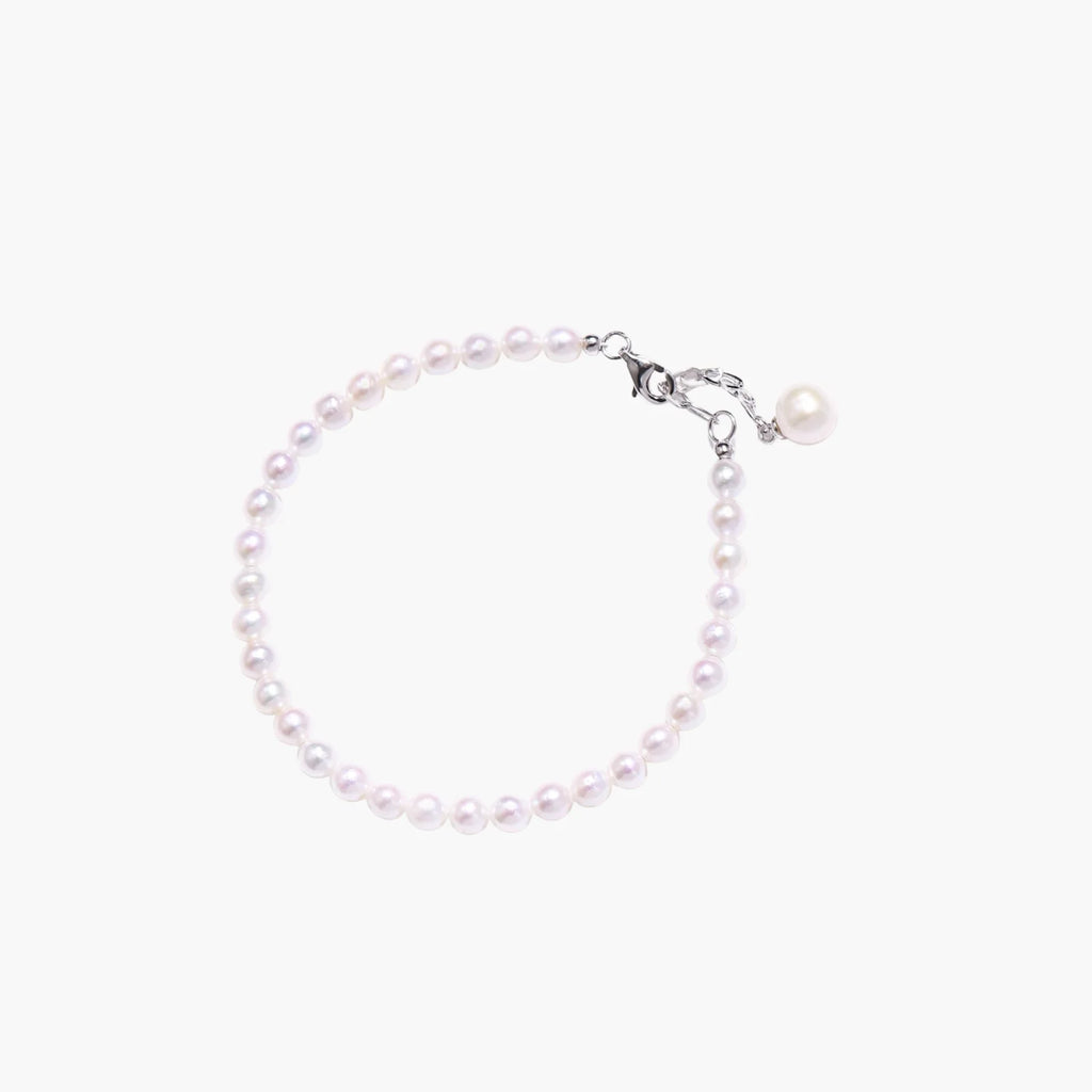 Delicate freshwater pearl bracelet with rhodium-plated silver clasp and single pearl drop charm on cream background