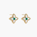 Gold quatrefoil stud earrings with white mother-of-pearl petals and emerald green gemstone center on beige background.