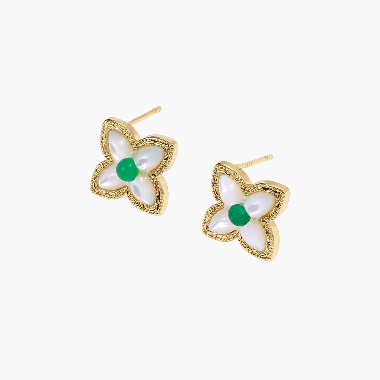 Gold quatrefoil stud earrings with white mother-of-pearl petals and emerald green gemstone center on beige background.
