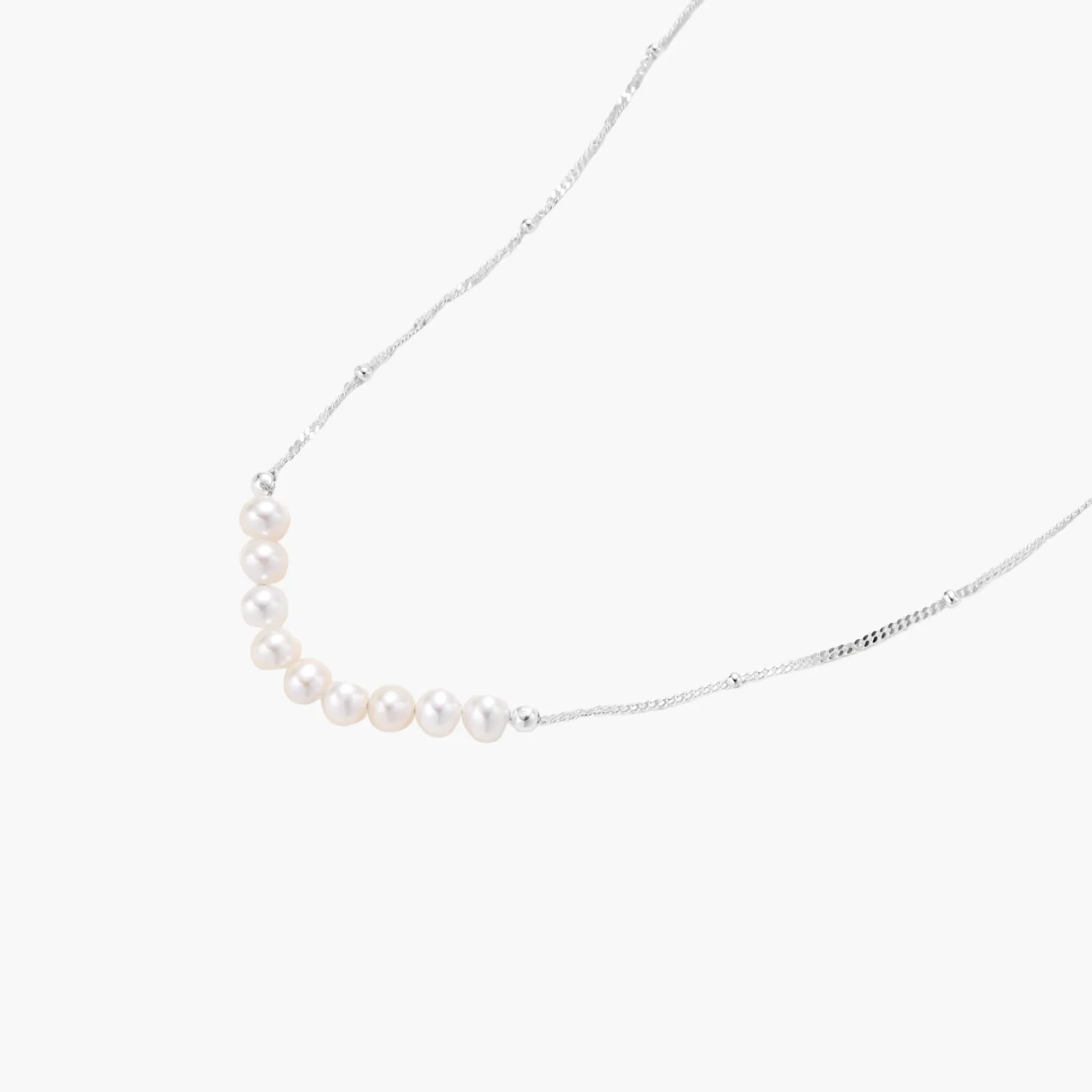Delicate sterling silver chain necklace with small freshwater pearls arranged in a curved smile arc on cream background.