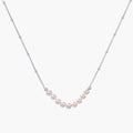 Delicate sterling silver chain necklace with small freshwater pearls arranged in a curved smile arc on cream background.