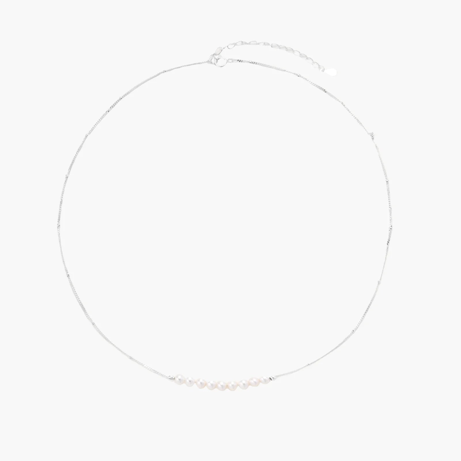Delicate sterling silver chain necklace with small freshwater pearls arranged in a curved smile arc on cream background.