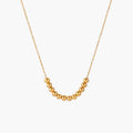 Delicate gold-plated necklace with graduated spherical beads forming gentle smile curve on beige background