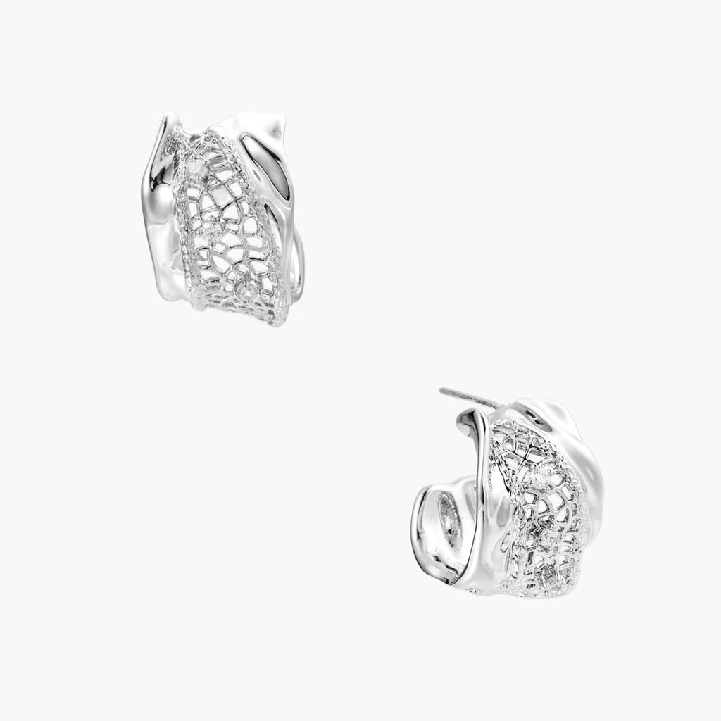 Close-up of sculptural hoop earrings with lattice center band and smooth twisted edges in white gold-plated brass with zirconia
