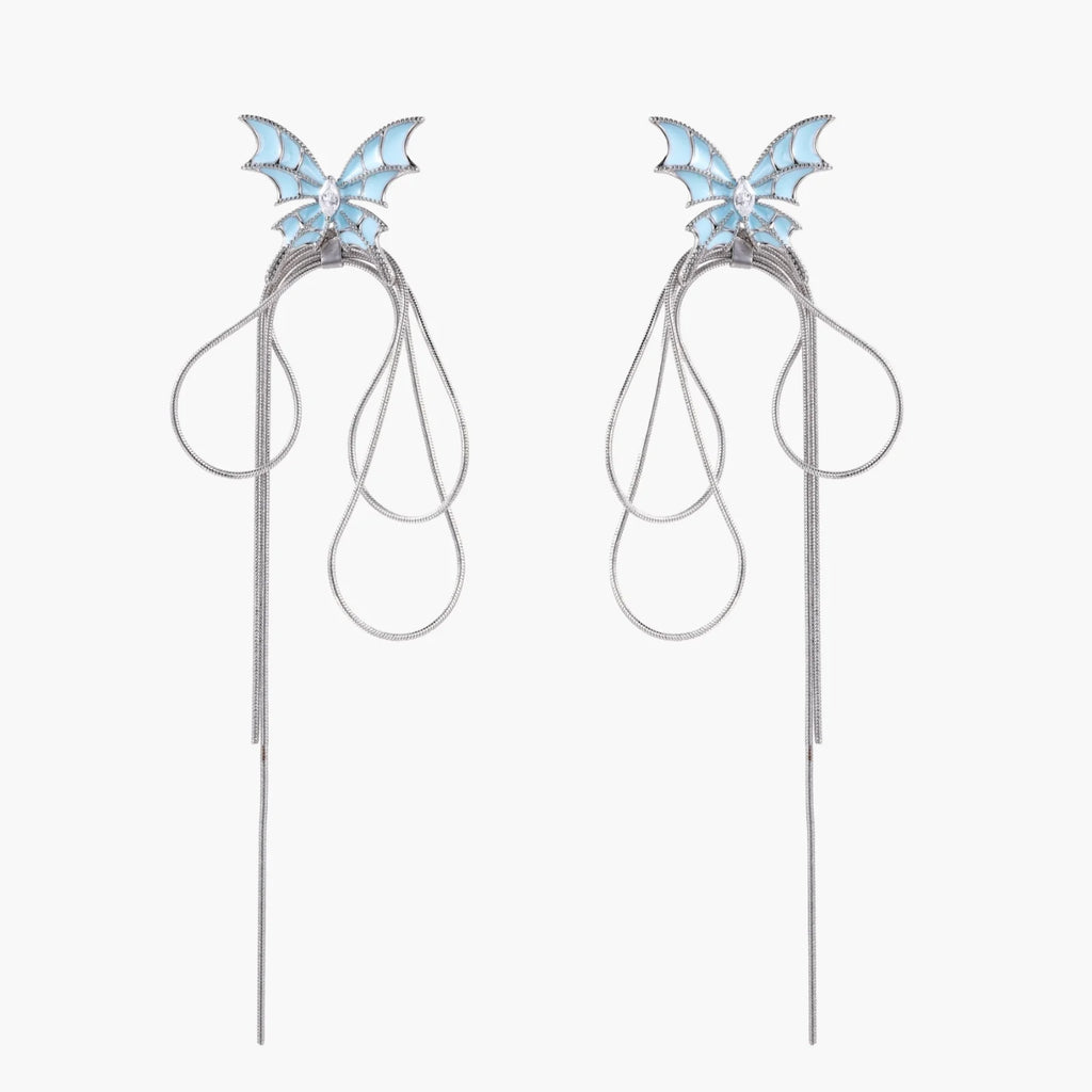 Long silver-tone earrings with powder blue enamel butterfly studs and flowing chain tassels on cream background