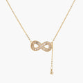 Gold infinity pendant with baguette crystals on adjustable chain against cream background.