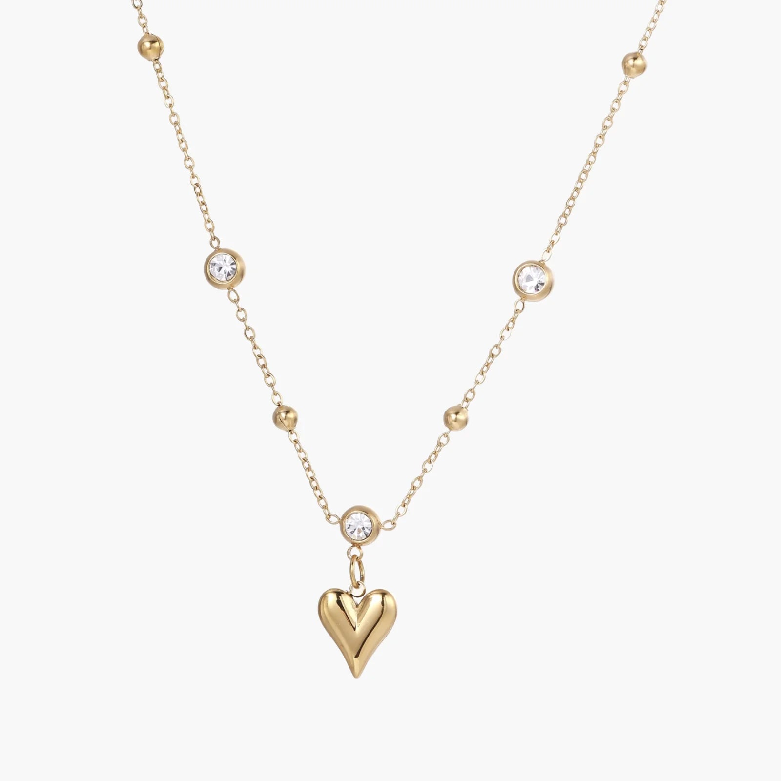 Delicate gold-plated necklace with bezel-set crystals and small heart pendant on beige background