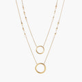 Layered gold necklace set with two open circle pendants and mixed chain styles on beige background