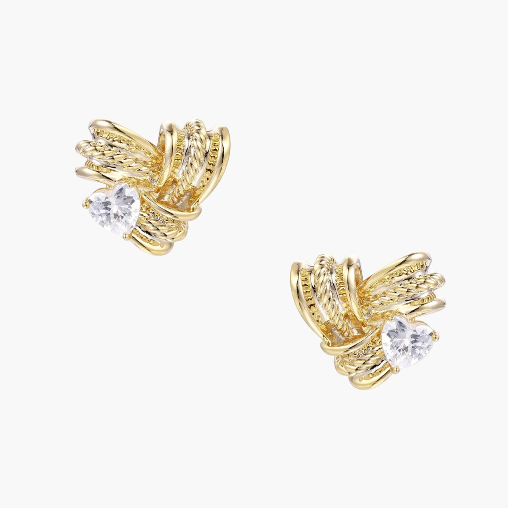 Pair of sculptural gold-plated wing stud earrings with zirconia stones on cream background, showing dimensional feather design