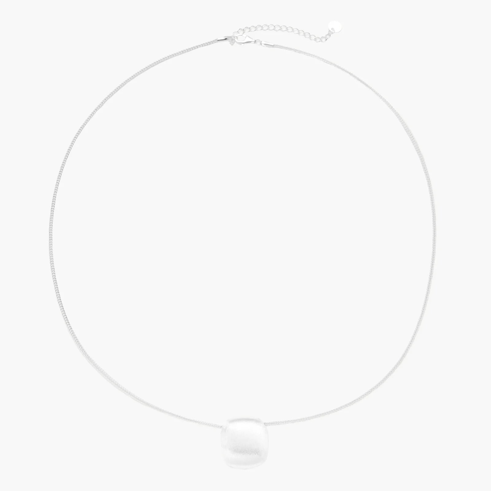 Minimalist brushed sterling silver dome pendant on delicate chain against cream background, showing matte textured finish