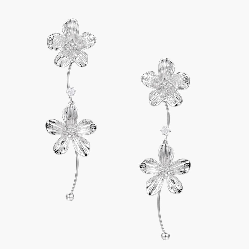 Silver-white asymmetric earrings with textured flower petals and crystal centers on cream background